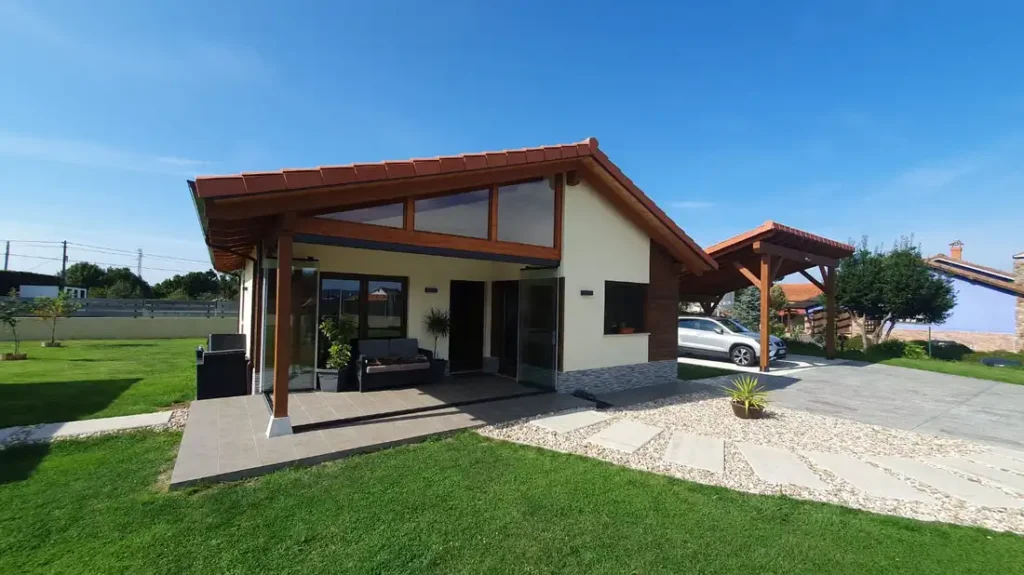 Porche acristalado en Muros de Nalón, Asturias, con mobiliario de exterior en ratán, vistas al jardín y techo de madera. Un espacio luminoso y acogedor ideal para relajarse.