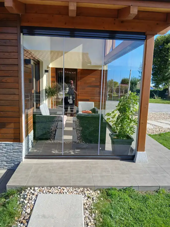Vista de un porche acristalado en Muros de Nalón, Asturias, con muebles de exterior modernos, techo de madera y jardín al fondo. Espacio diseñado para disfrutar de la luz natural y la comodidad en cualquier época del año.