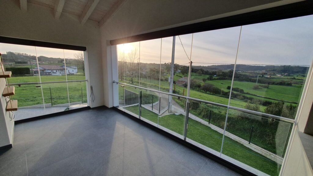 Porche acristalado en Luanco con cristales Lumon a large glass window with a view of a grass field