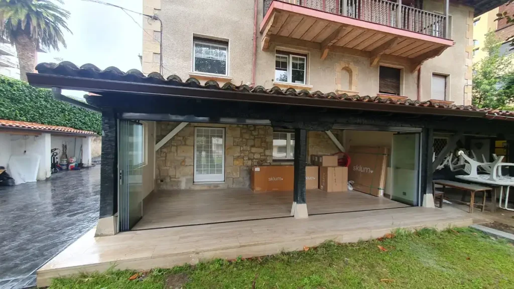 En esta vivienda tradicional ubicada en Castro Urdiales, nuestro equipo ha llevado a cabo el cerramiento completo de un porche con sistema de cortina de cristal sin perfiles verticales. Esta solución permite disfrutar del espacio exterior durante todo el año, protegido del viento, la lluvia y el frío, sin perder la conexión visual con el jardín. El cerramiento acristalado se ha integrado respetando la estética rústica de la vivienda, conservando el estilo del porche original gracias a su diseño discreto y elegante. El sistema Lumon empleado es completamente abatible y deslizante, lo que facilita su apertura total en los meses de buen tiempo. Una instalación práctica, estética y duradera, ideal para quienes buscan ampliar su vivienda de forma funcional y eficiente.