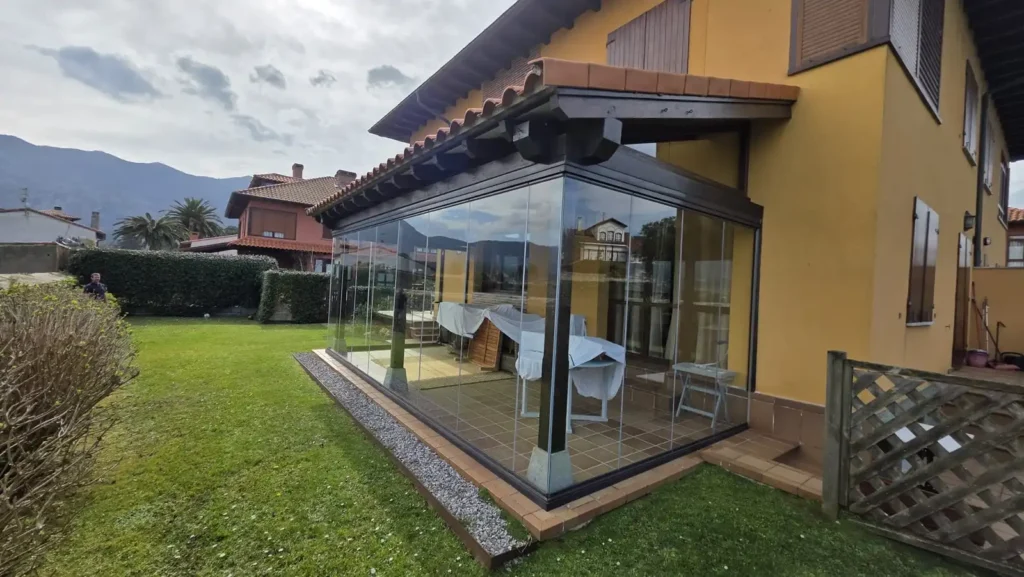 Instalación de sistema acristalado en porche en La Isla, Asturias. Protección frente al viento y la lluvia sin perder vistas ni luminosidad.